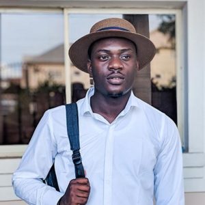 young man wearing a white shirt, a brown fedora hat, and carrying a backpack